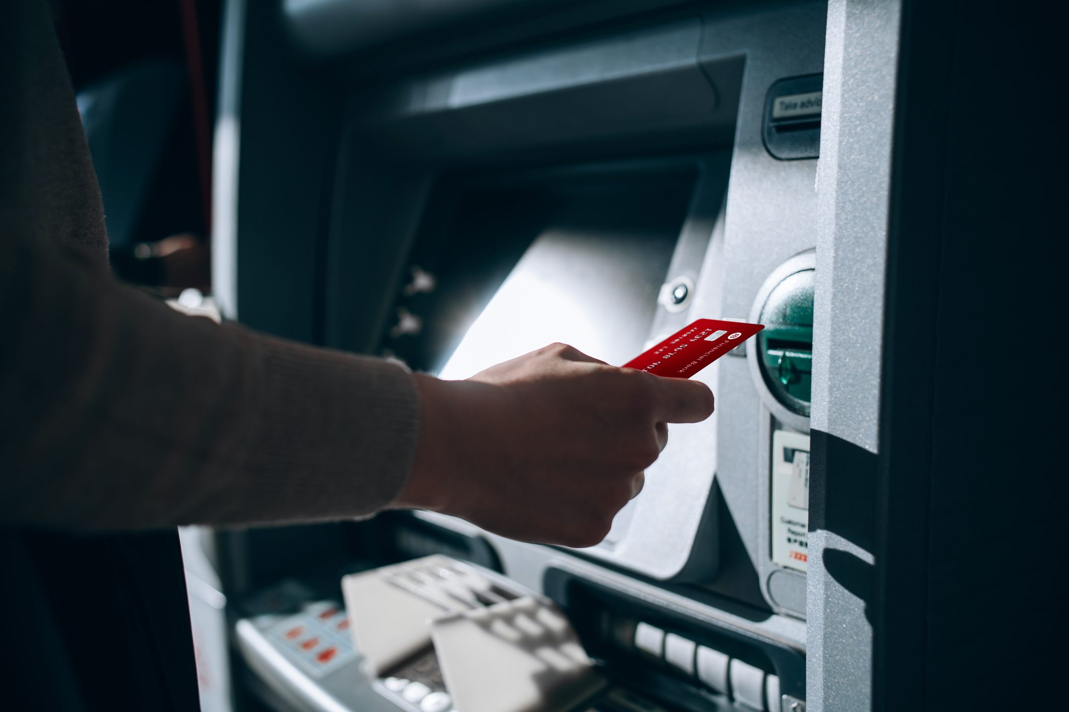 Close up of young woman inserting her bank card into automatic cash machine in the city. Withdrawing money, paying bills, checking account balances, transferring money. Privacy protection, internet and mobile security concept