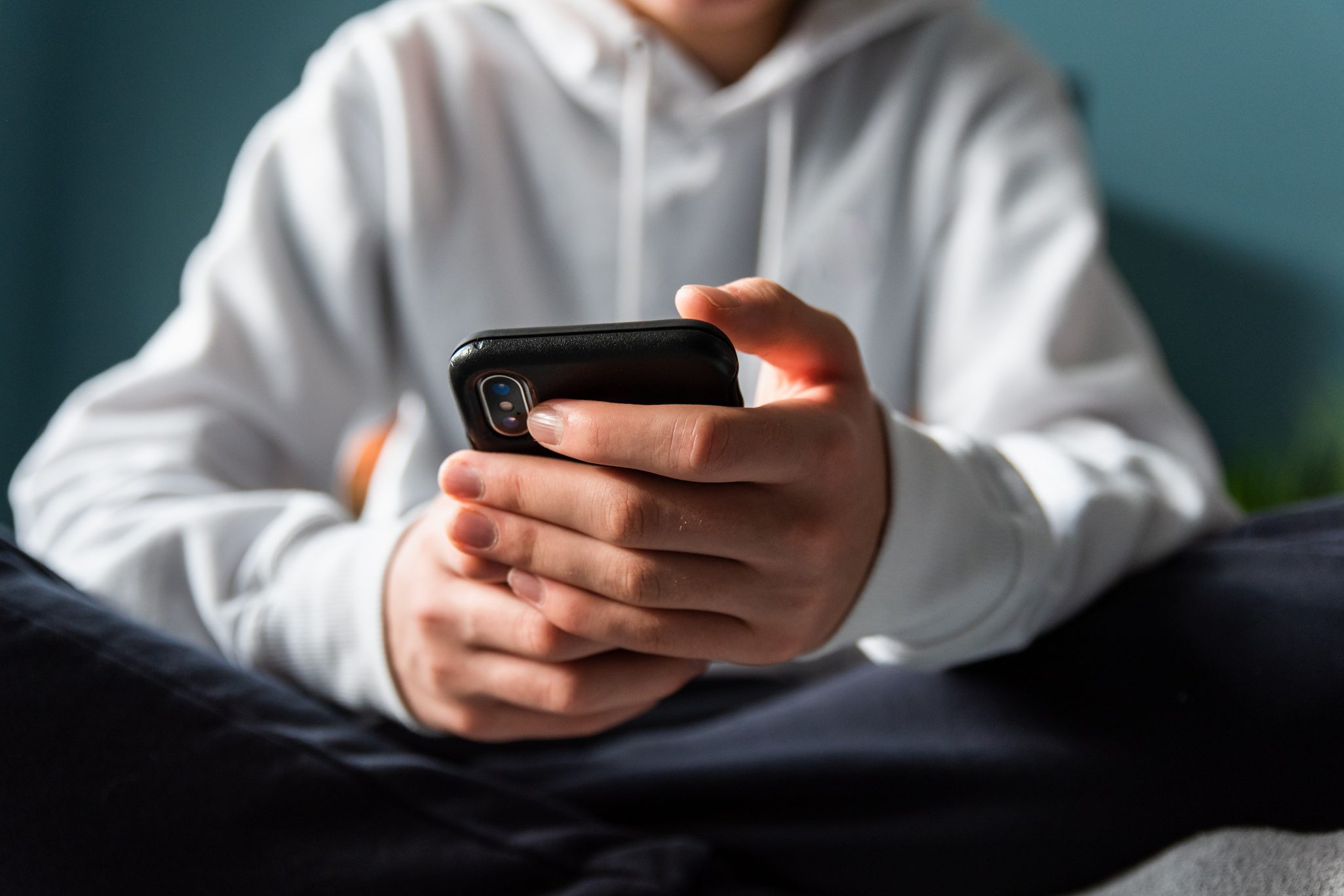 Close up of hands of teen boy in white sweater texting on phone.