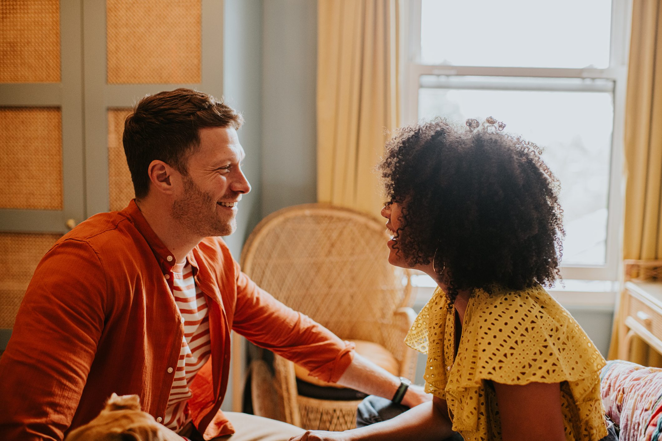 A couple in a stylish bedroom have an animated, and lighthearted discussion.