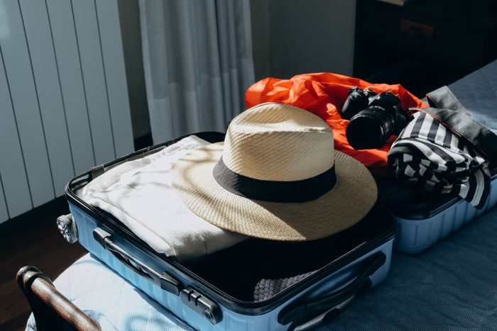 Summer clothes in a suitcase luggage for travel, Shadow Overlay . French style T-shirt with stripes and straw summer hat.