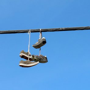 two pairs of old Sneakers on an Overhead power line Wire against a cloudless blue sky