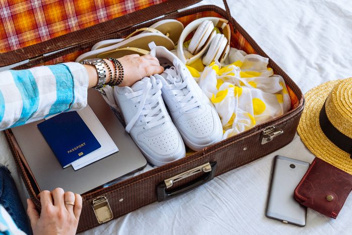 woman hands with watch put clothes in suitcase. travel concept. copy space. biometric passport laptop wallet