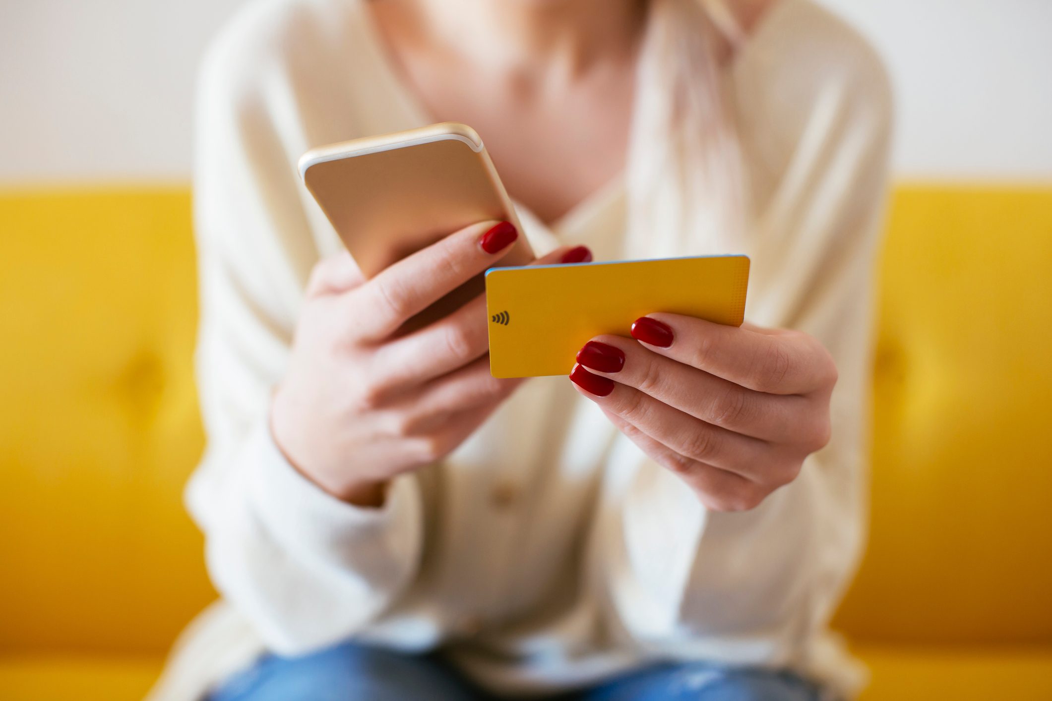 Blonde woman using smartphone and using bank card at home