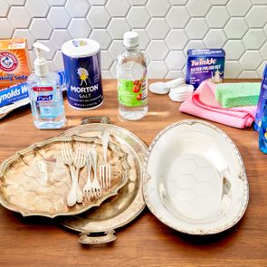 A countertop with household supplies you can use to clean tarnished silver, with tarnished and polished silver to show the before and after