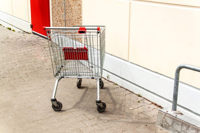 Empty shopping cart near the supermarket wall. Parking at the supermarket. Shopping symbol. Metal cart.