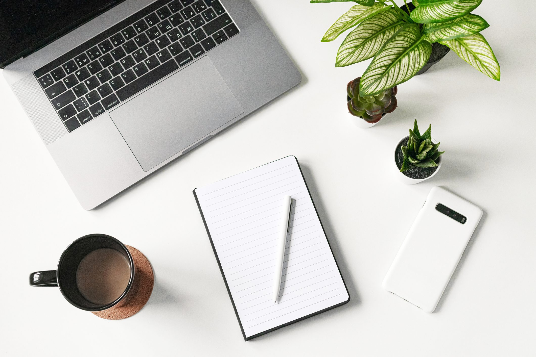modern white office desk table with laptop, smartphone and blank notebook and cup of coffee, flatlay, top view workspace, business
