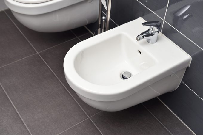 White bidet screwed to a gray tiled wall in the bathroom, close-up