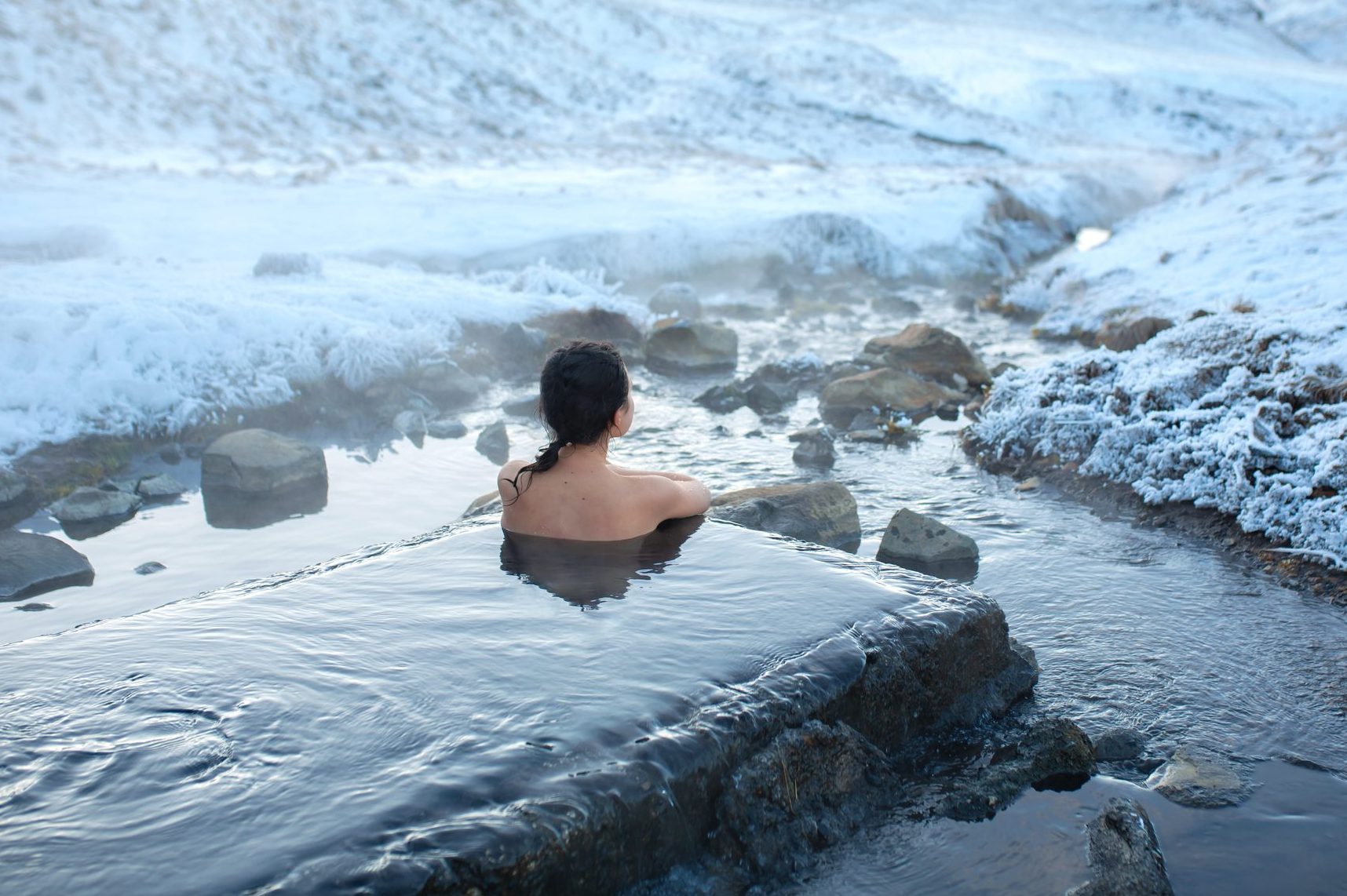 The girl bathes in a hot spring in the open air with a gorgeous view of the snowy mountains. Incredible iceland in winter