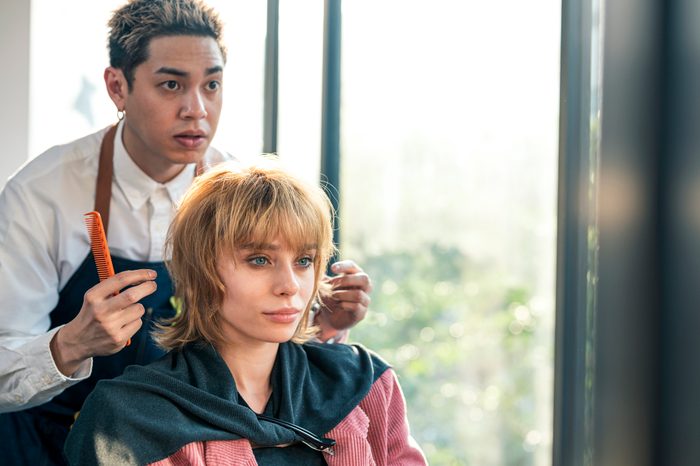Asian hairdresser owner is giving advice about hairstyle to his customer at hair salon.