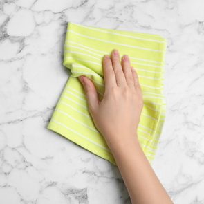 Woman wiping white marble table with kitchen towel, top view. Space for text