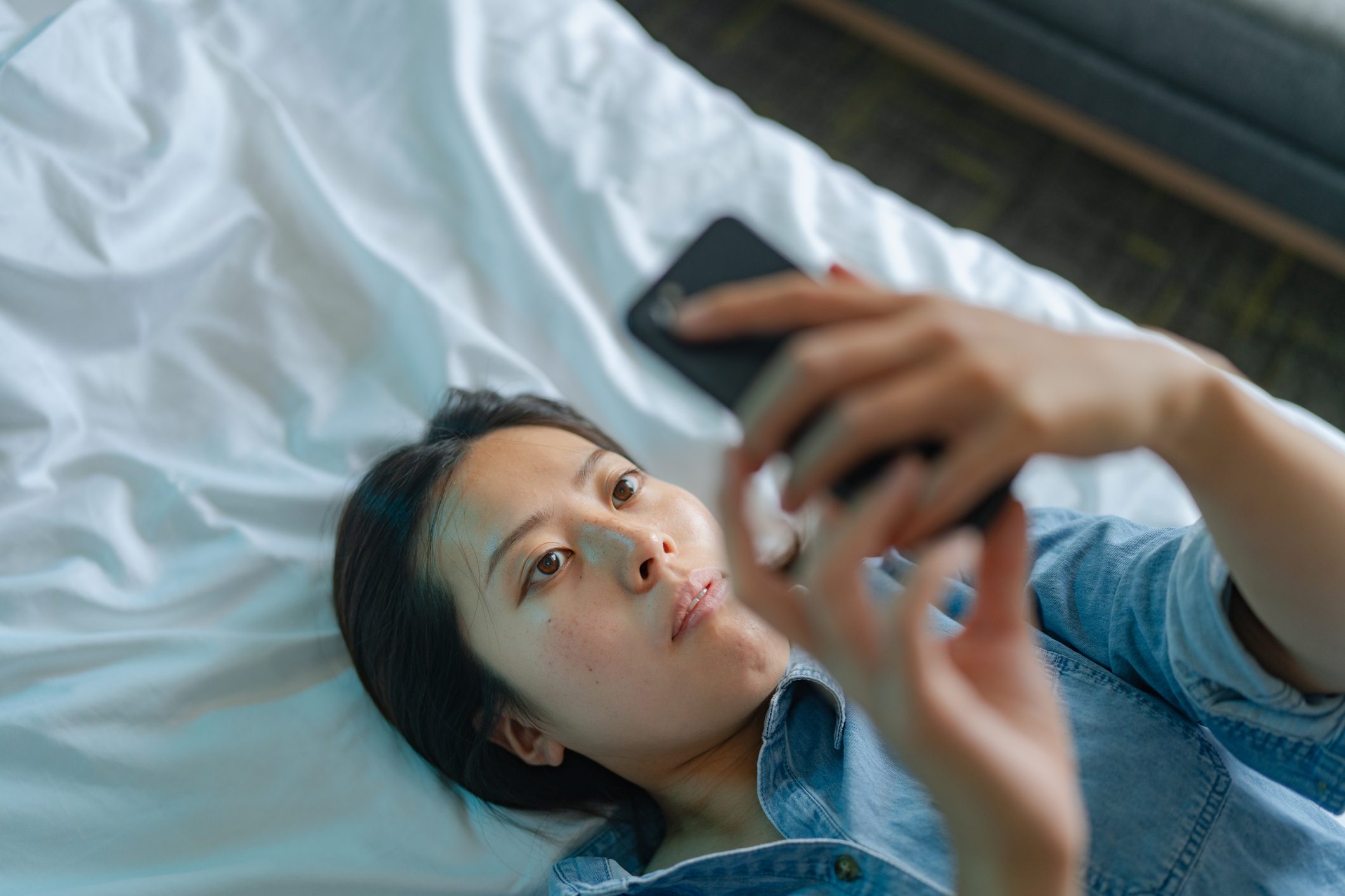 High angle view of young woman using smart phone while lying down on her bed