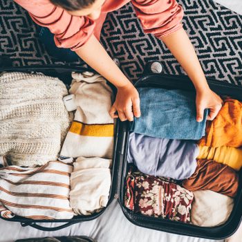 Happy woman packing suitcase in bedroom.