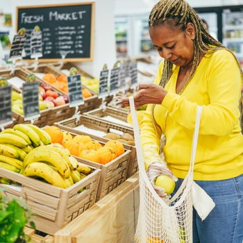 African female customer buying organic food fruits inside eco fresh market - Focus on box of oranges