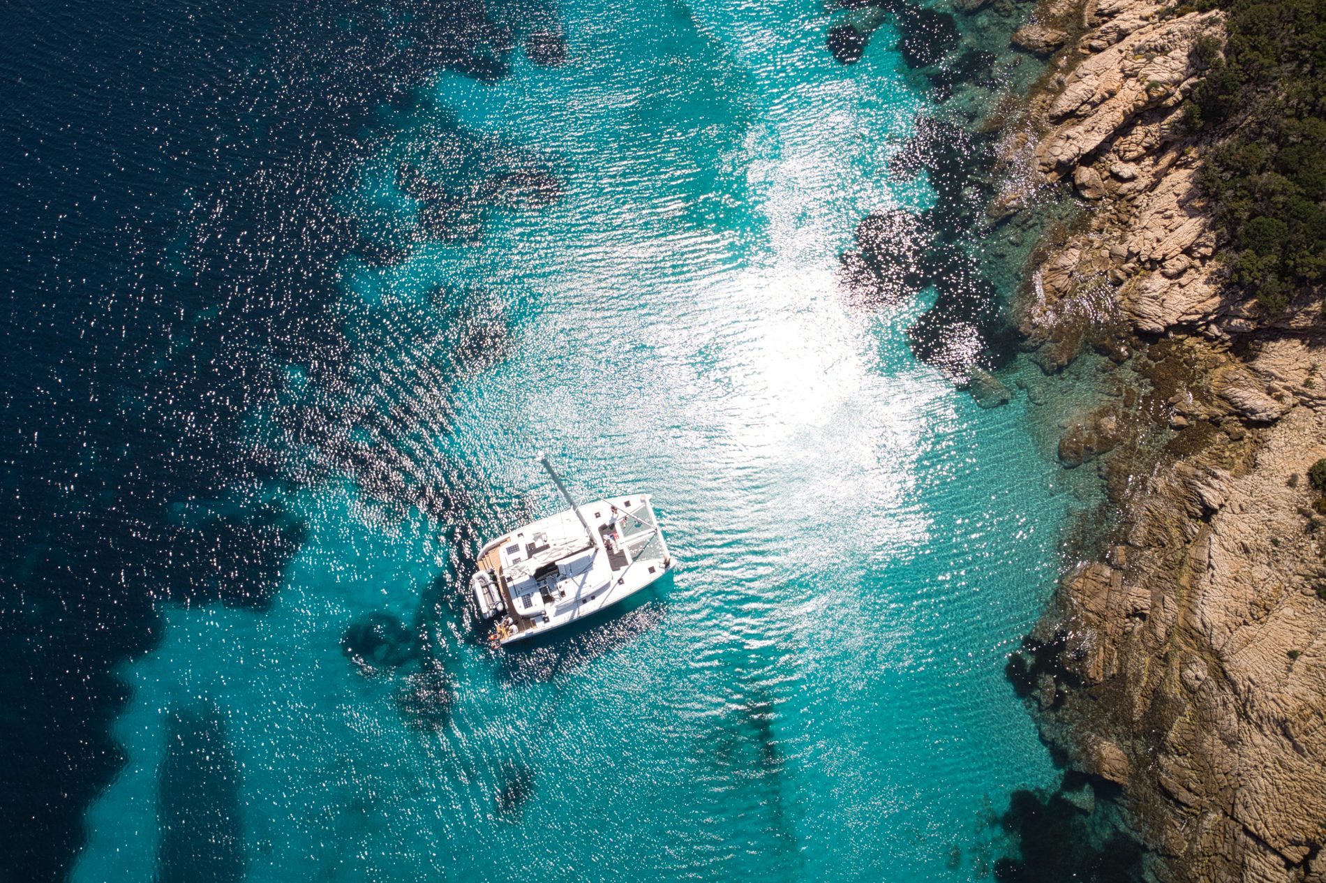Bird's eye view of a white boat, swimming in the blue, shining sea under the sunlight