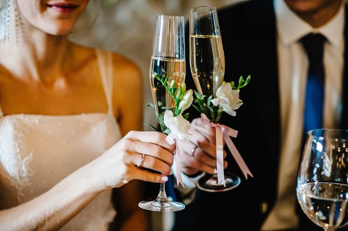 Glass decorated with flowers and greenery on the background newlyweds. close up. The bride and groom hold glasses of champagne in their hands. Wedding ceremony.