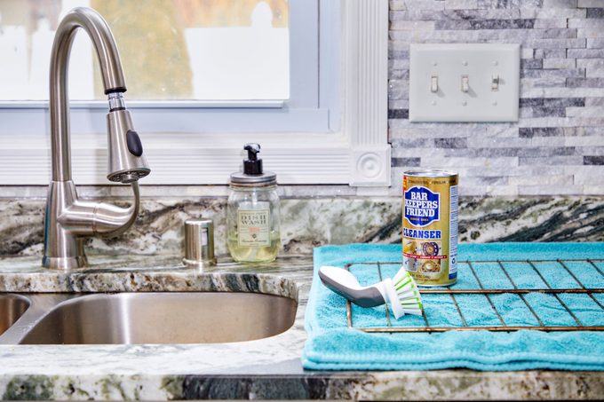 oven rack and cleaning supplies laid out near a kitchen sink