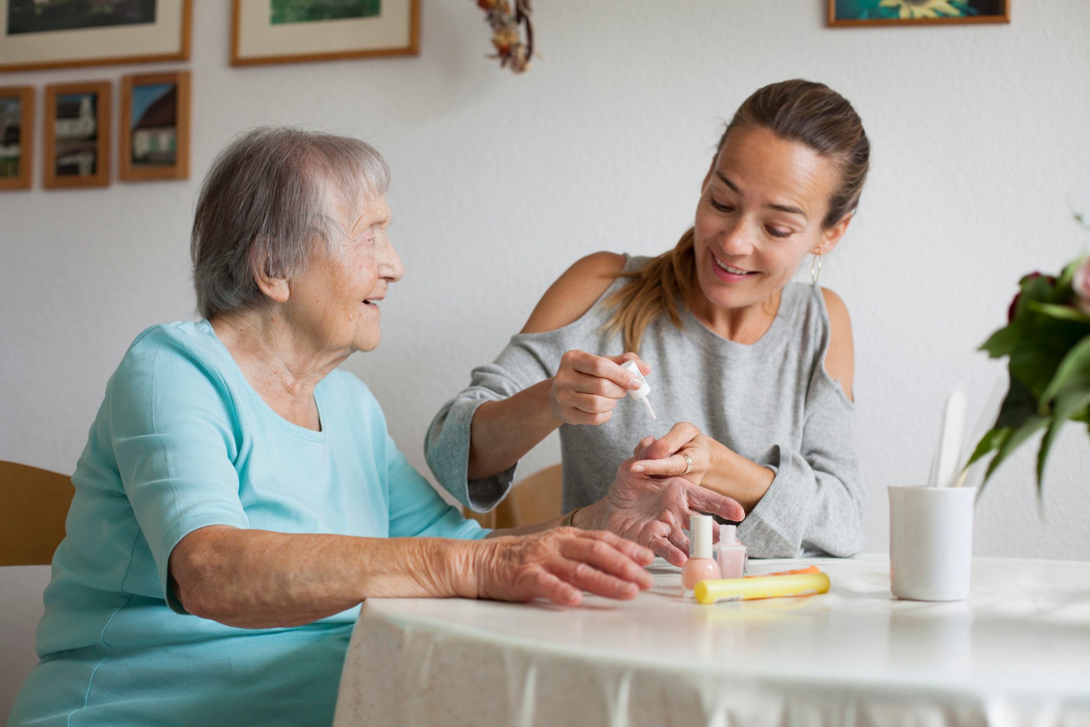 Senior woman and her adult granddaughter sitting at kitchen table doing manicure