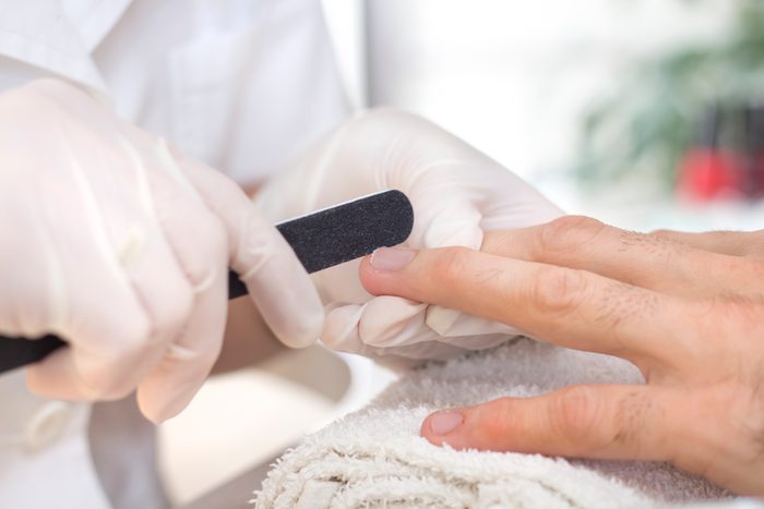 Beautician in white disposable gloves in a beauty salon during a manicure treatment manicures his nails with a nail file