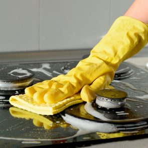 In a yellow rubber glove, a hand cleans a gas stove. Kitchen cleaning