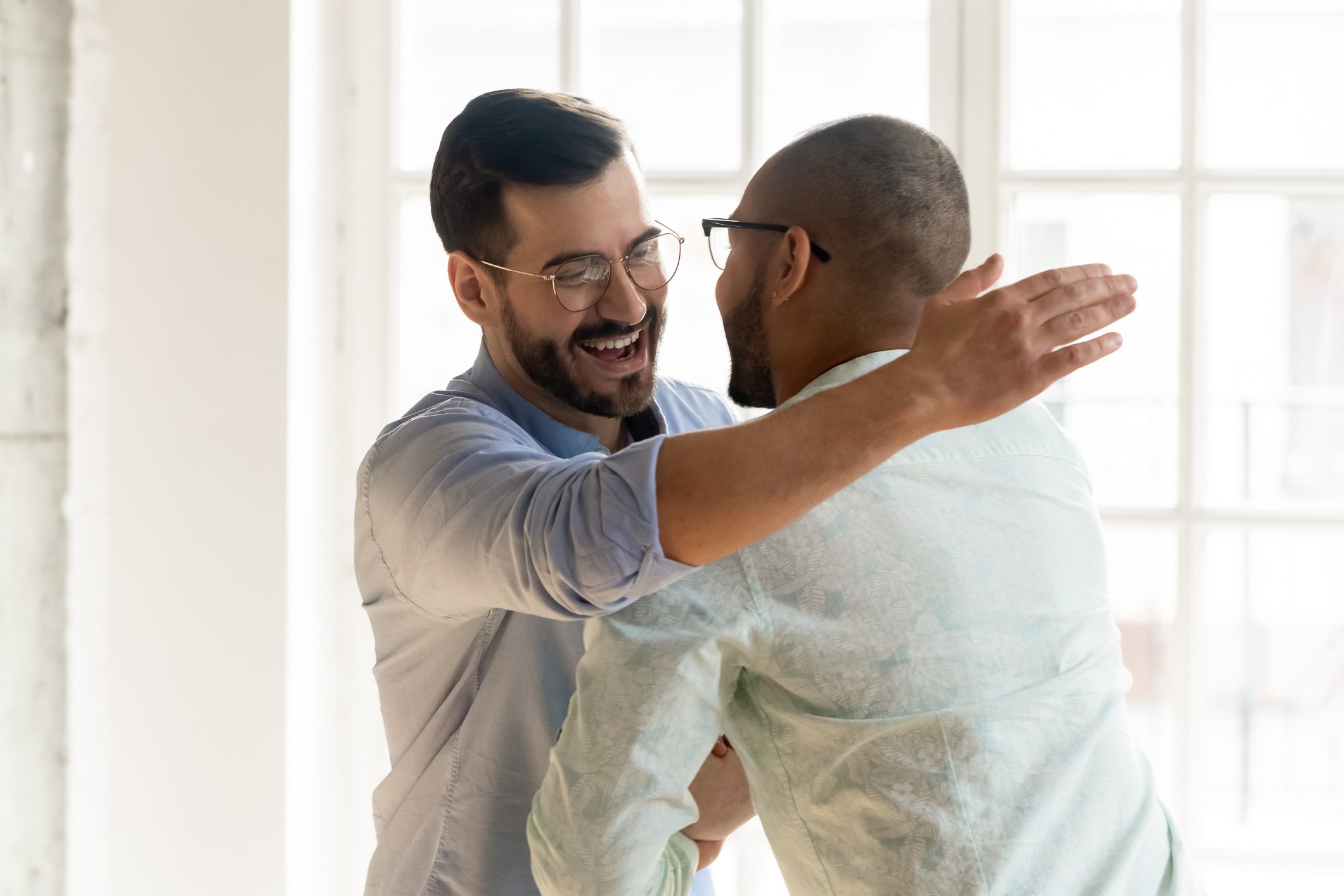 Smiling male friends embrace tap shoulder meeting indoors