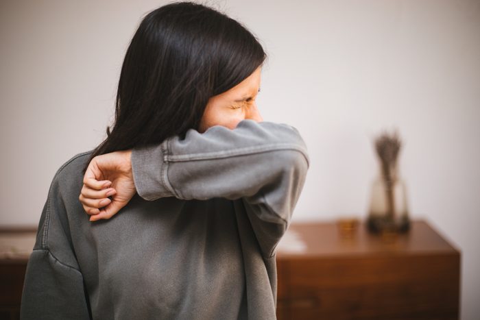 young woman sneezing into the inside of her elbow in a nail salon