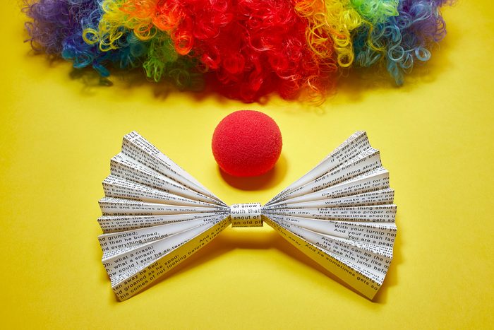 origami bowtie made from funny poetry page, red clown nose, and rainbow clown wig on yellow background