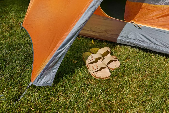 slide sandals sitting right outside the door of an orange tent in the grass