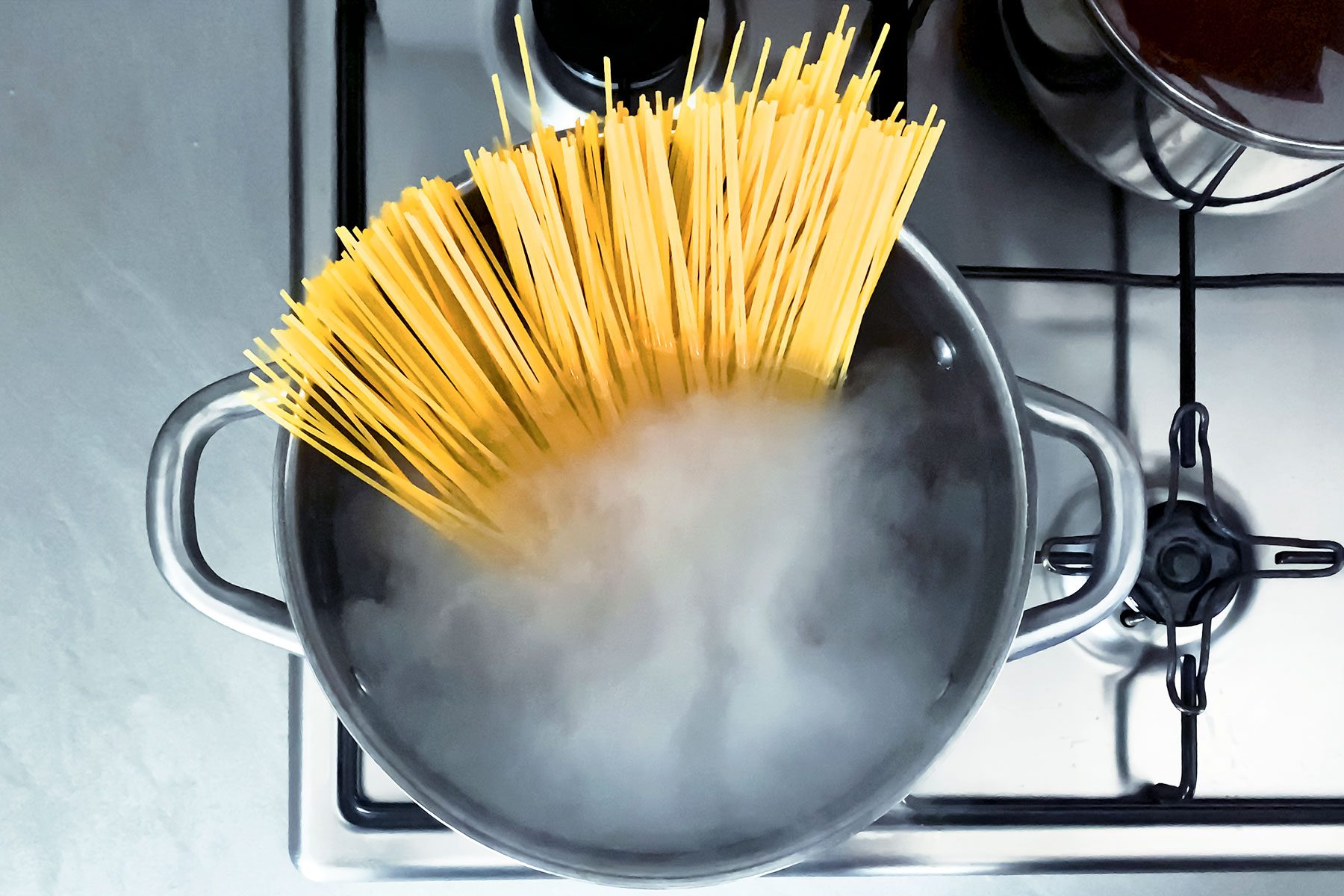 Cooking raw spaghetti in the boiling water contained in a saucepan