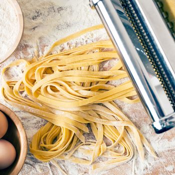 fresh pasta, eggs, flour and pasta machine on kitchen table