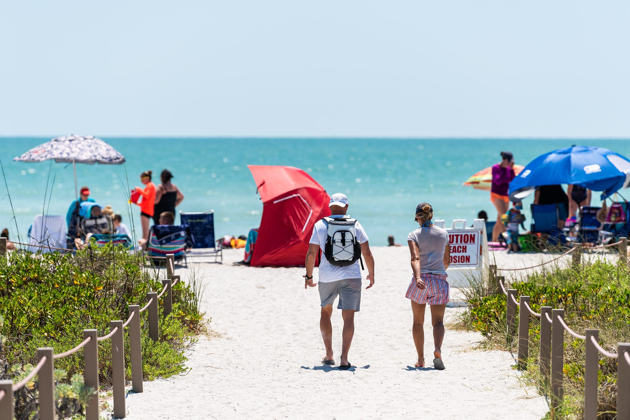couple walking on sandy trail path walkway by fence to Bowman's beach, Sanibel Island, Florida, USA, with other beachgoers in the background