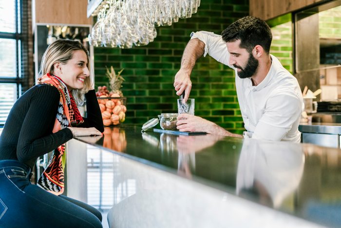 Smiling woman at the counter of a bar watching barkeeper preparing a cocktail