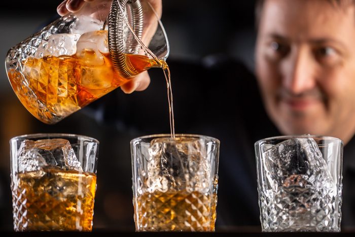 Whisky bourbon on ice being prepared by a professional bartender pouting the drink into ornamental glasses.