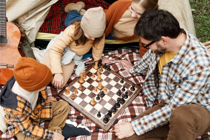 Happy smiling family playing chess game at campsite during camping trip in nature