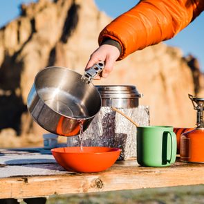 Pouring water from a pot while cooking with a camp stove on a picnic table