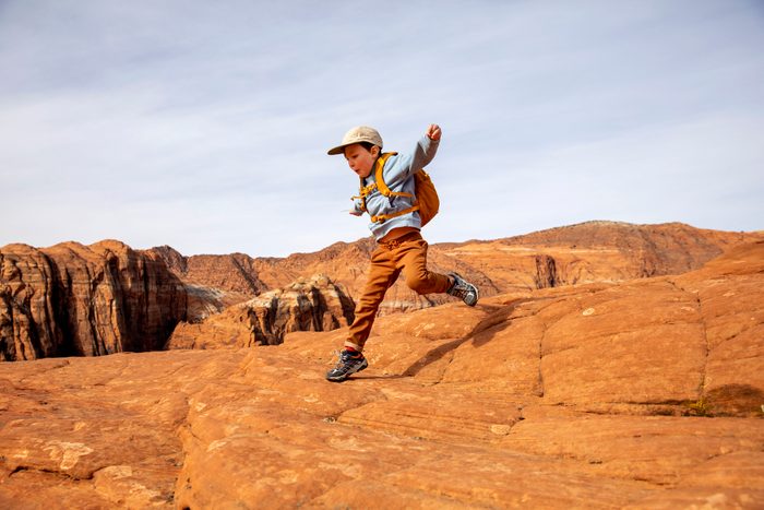 A young boy jumping off a rock while hiking.