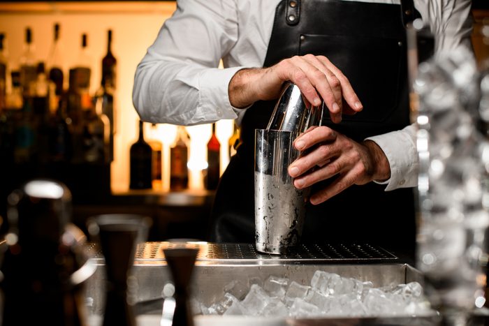 selective focus on shiny steel shaker on the bar counter, which is held by the hands of a male bartender