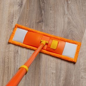 Orange mop washing dusty floor at home. Cleaning the wooden laminate floor with wet microfiber mop. Mopping the floor. Housekeeping, homework routine, cleaning concept.