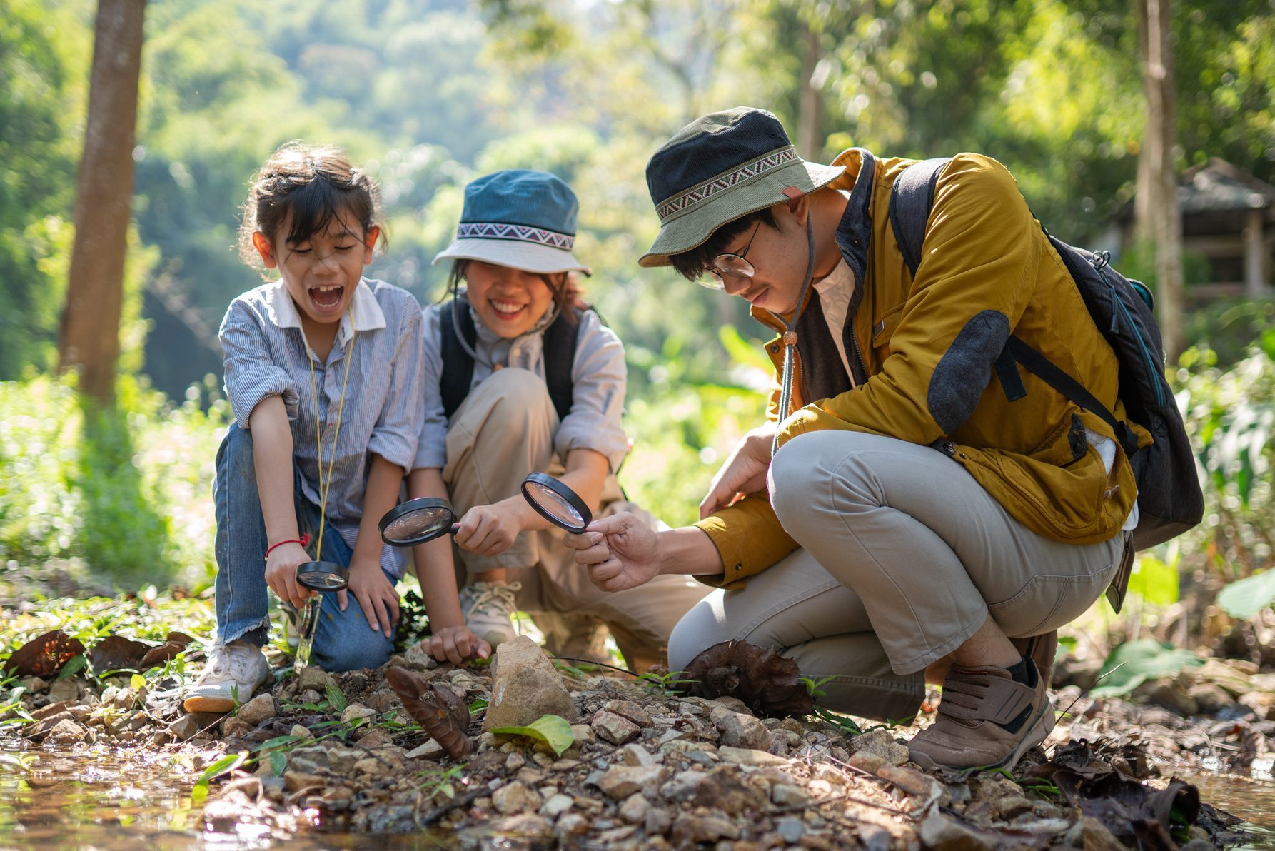 Children in the forest look at the rock as a researcher with a magnifying glass.