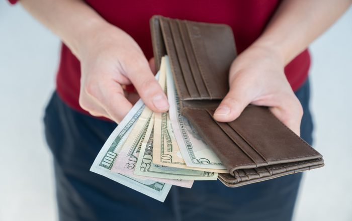 Cropped shot of someone while keeping American dollar banknotes in leather wallet.