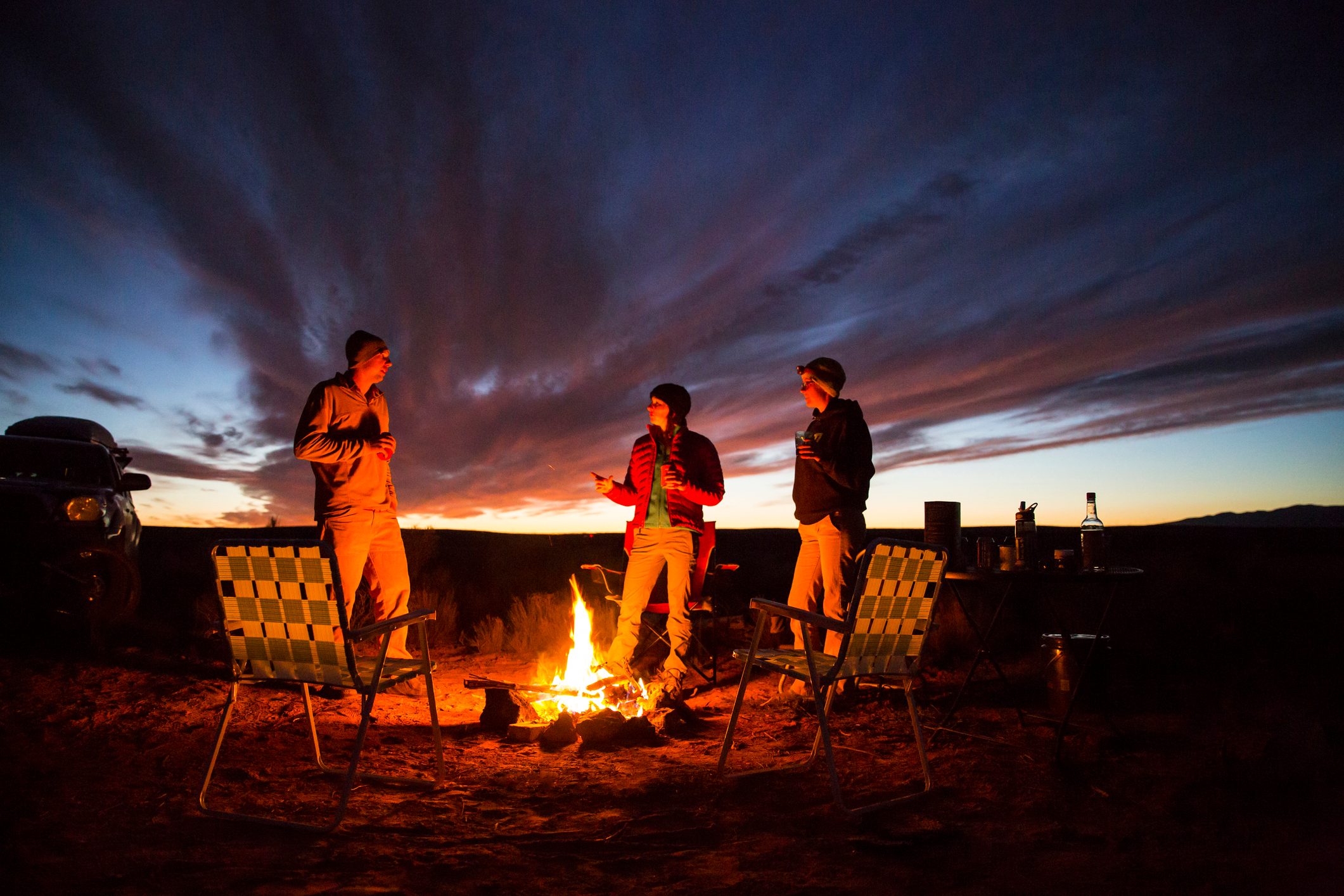 Three friends handing out at a campfire.