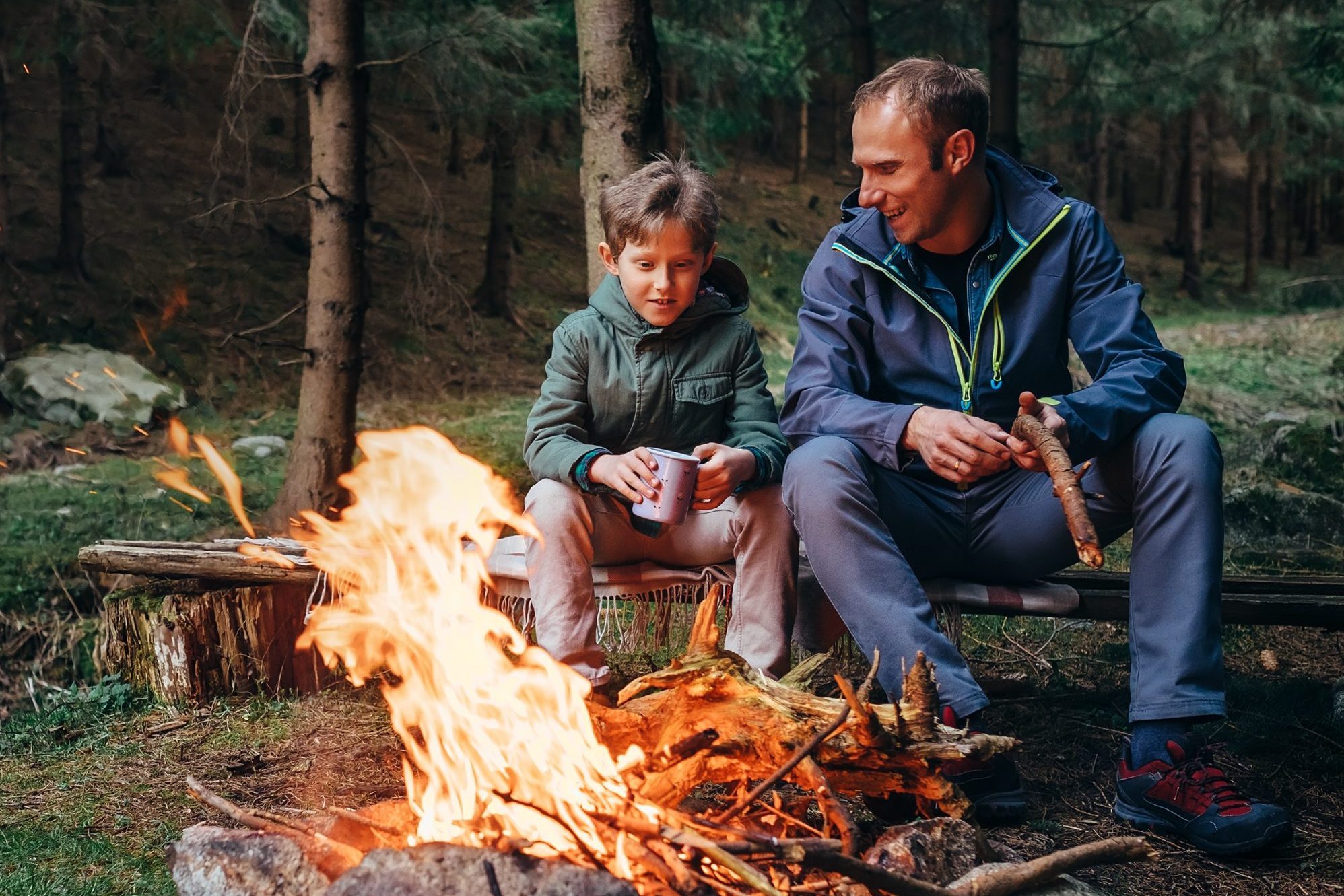 Father with son warm near campfire, drink tea and have conversation