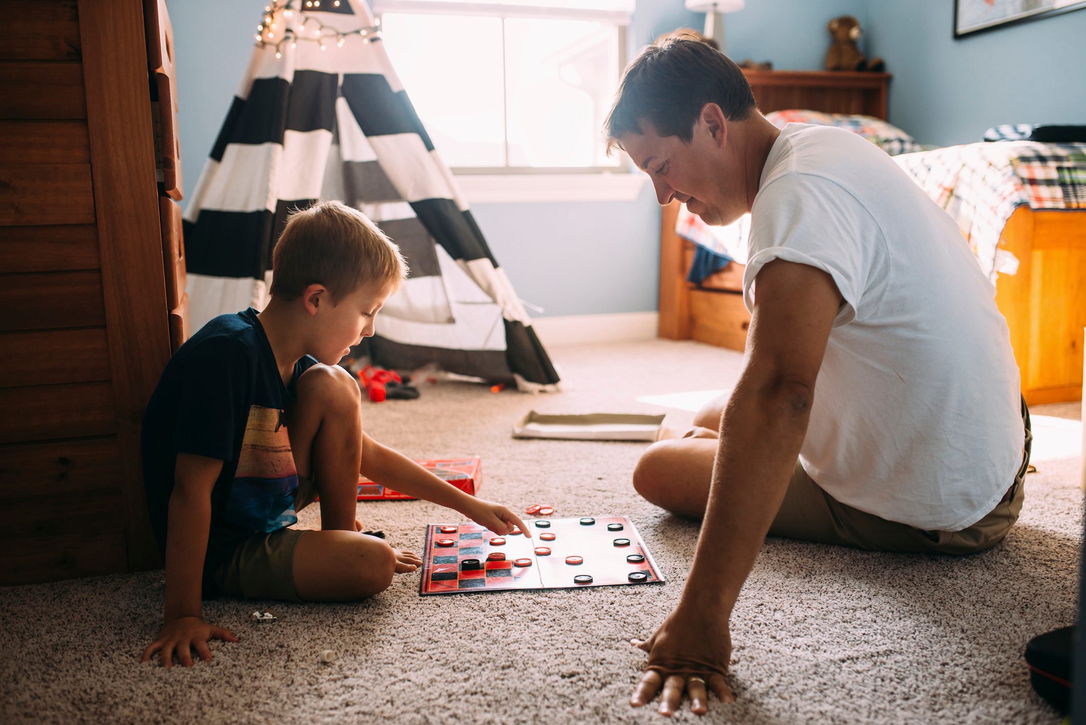 Father and son playing checkers while sitting on carpet at home