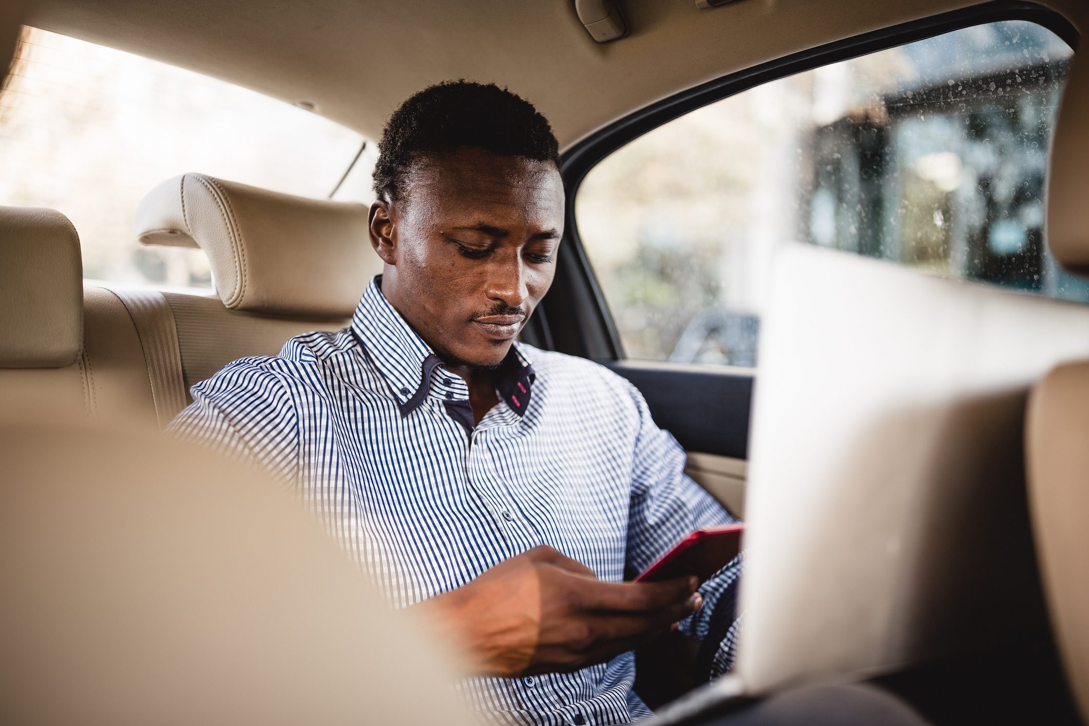 African businessman in taxi, using laptop and mobile phone on the back seat.