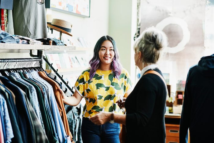 Smiling shopkeeper helping client shop in clothing boutique