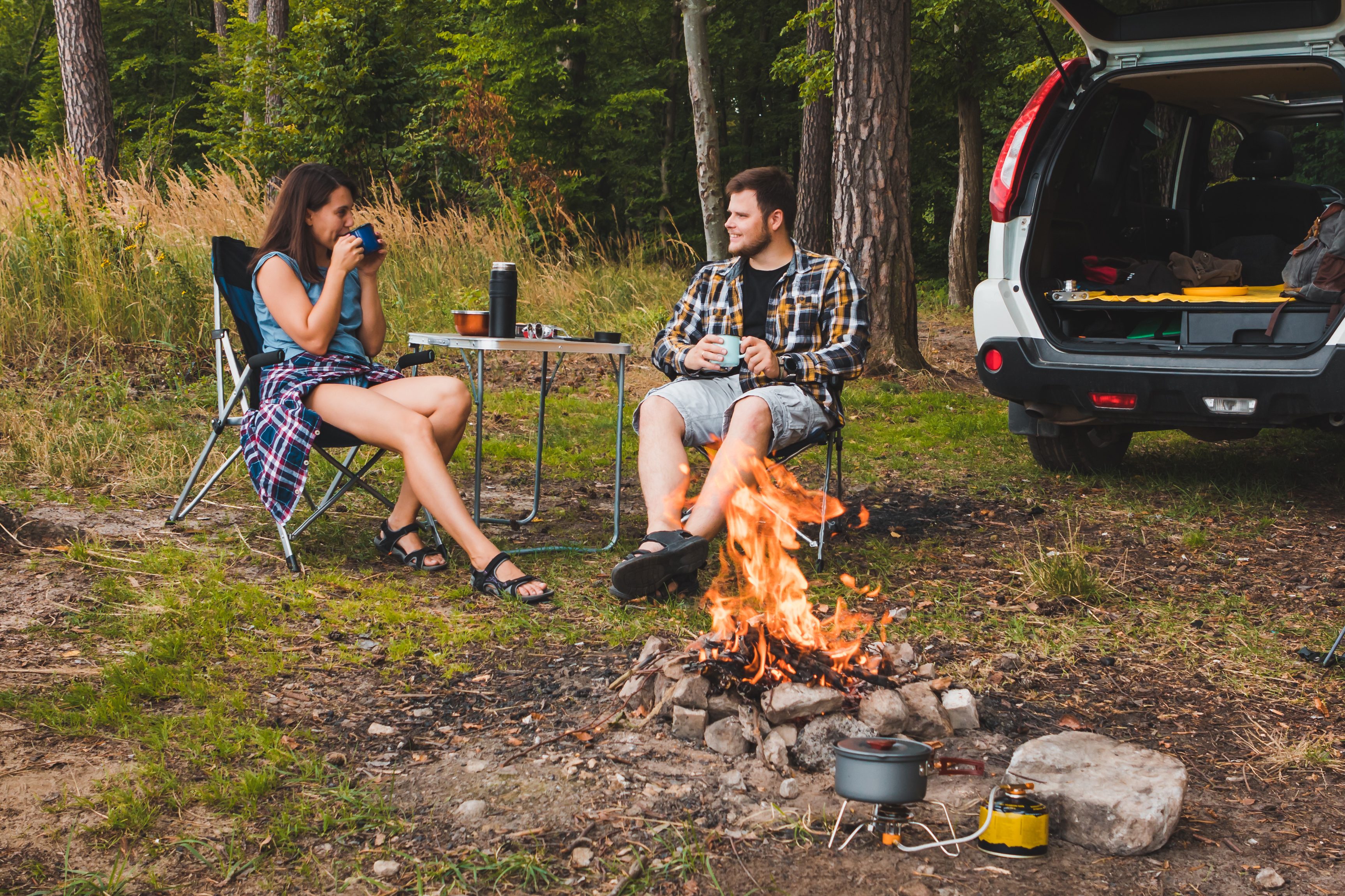 couple sitting in portable chairs drinking tea talking. camping summer activities