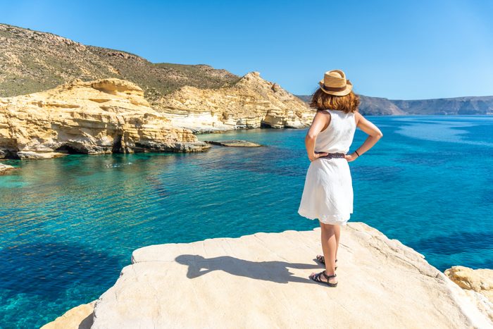 A young woman in a white dress looking at the sea in Rodalquilar in Cabo de Gata on a beautiful summer day, AlmerÃa. Mediterranean sea, spain