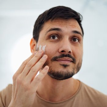 Handsome Man Applying Face Cream on his Cheek in the Bathroom