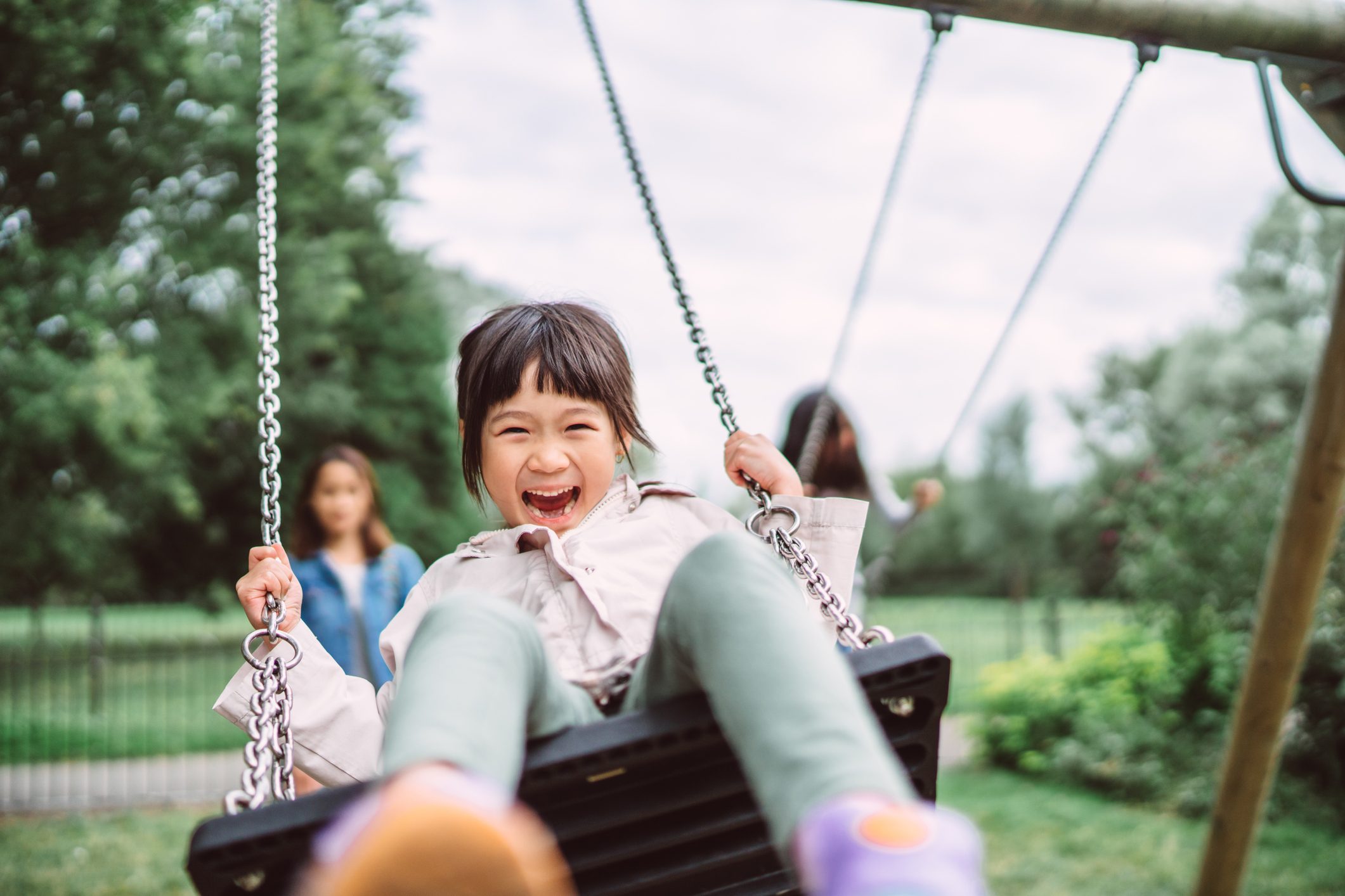 Lovely little girl smiling at the camera while playing on a swing set in playground joyfully