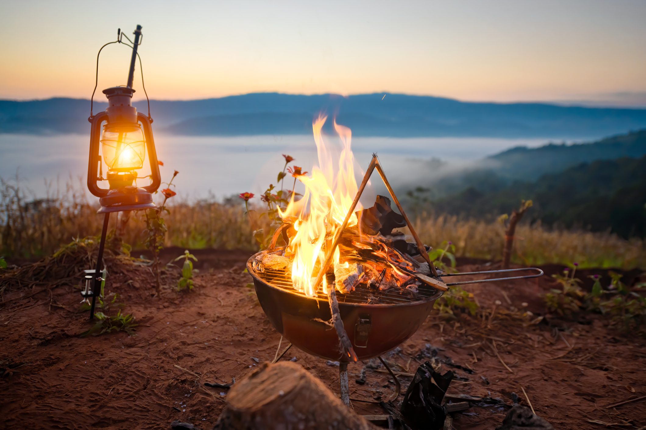 Camping fire burning in the morning light along with the mist foggy flowing between the mountain hill in background