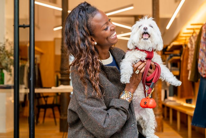 Cheerful woman carrying cute dog in front of clothing store